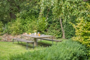 An outdoor dining area with a wooden table and benches, surrounded by lush greenery and trees. - 5 Bed in Potto (oc-t46322) (Potto)