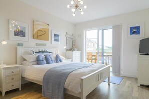A bedroom with a bed, bedside tables, a dresser, a television, and a balcony with a view. - 3 Bed in Porth (oc-b584338) (Newquay)