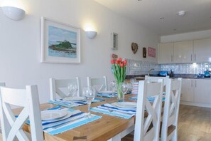 A dining area with a wooden table set for four, white chairs, and a vase of red tulips. - 3 Bed in Porth (oc-b584338) (Newquay)