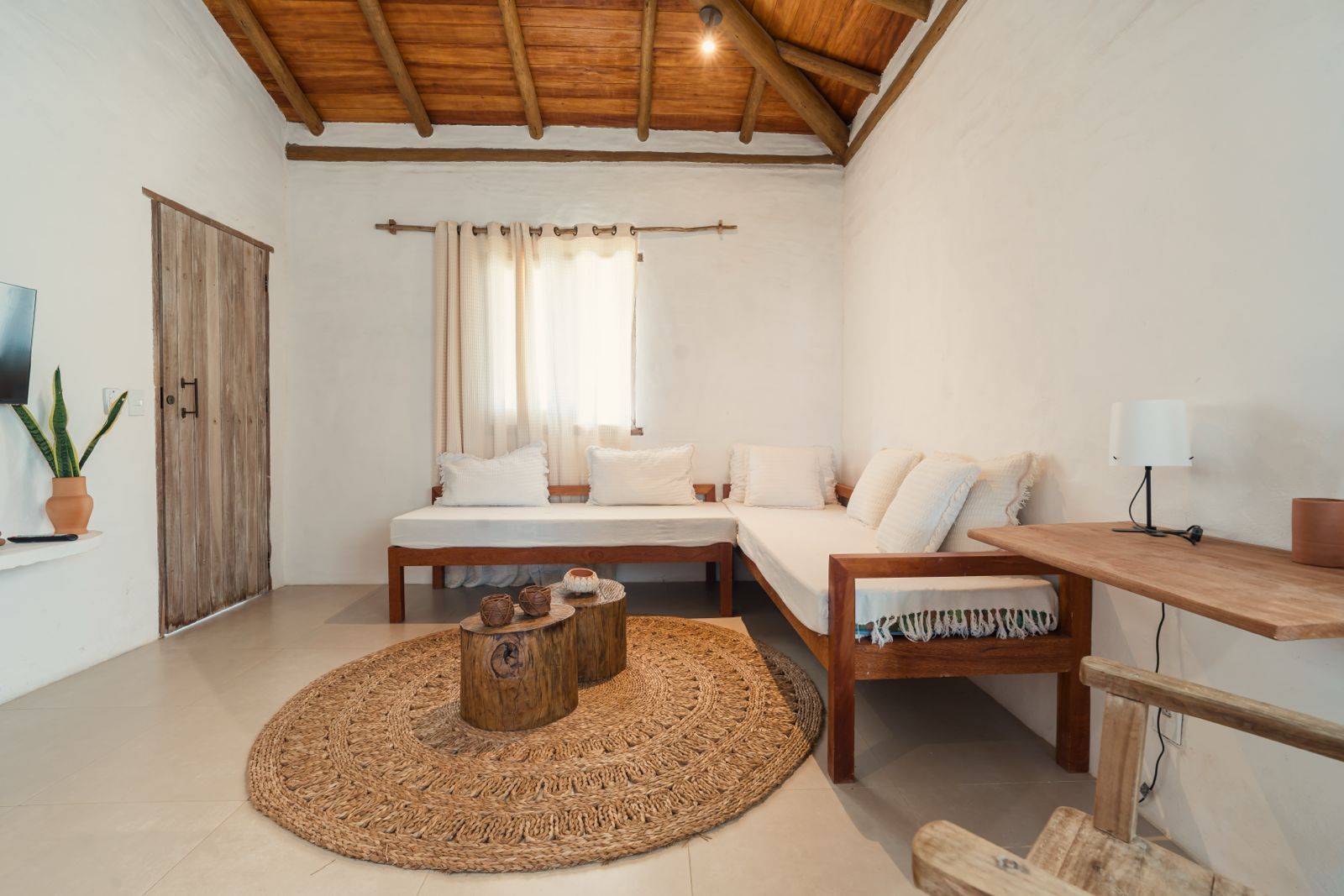 Ein modernes Schlafzimmer mit Holzboden, einem Bett mit weißer Bettwäsche, einem Nachttisch aus Holz, einem gewebten Teppich und einem Blumentopf.