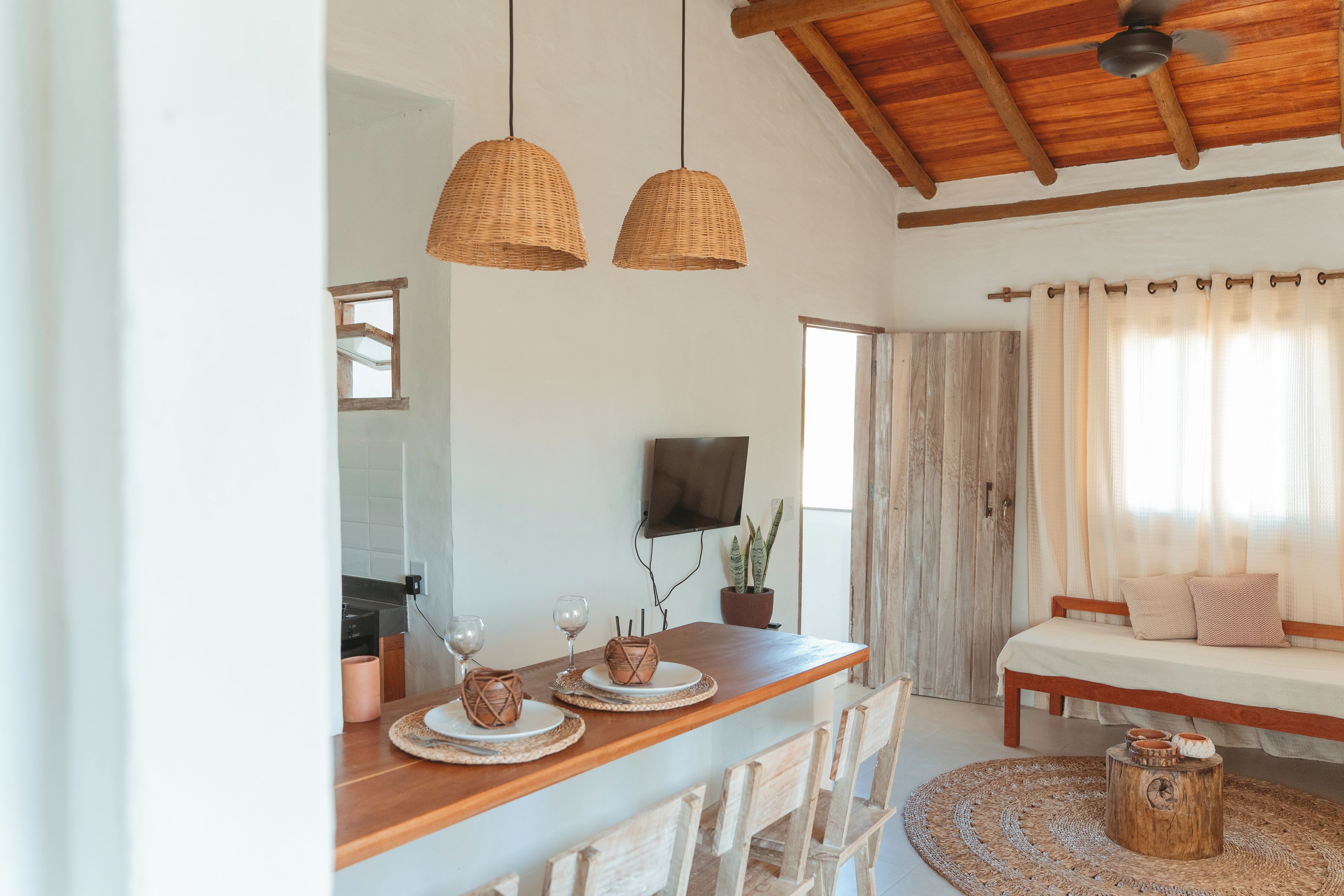 Comedor con mesa de madera, sillas y lámparas de mimbre colgantes.