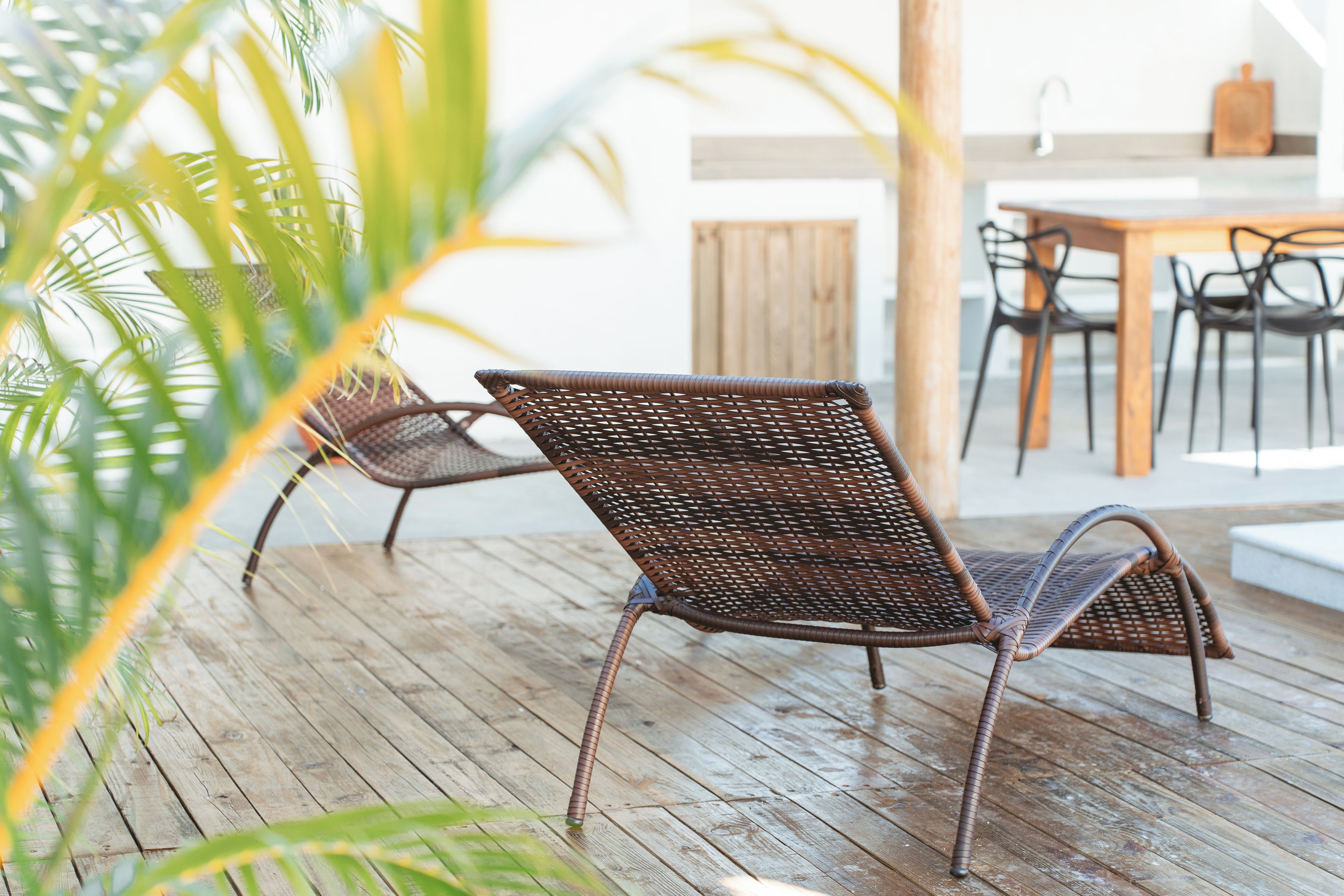 Een rieten stoel op een houten terras, met in de verte een eetgedeelte.
