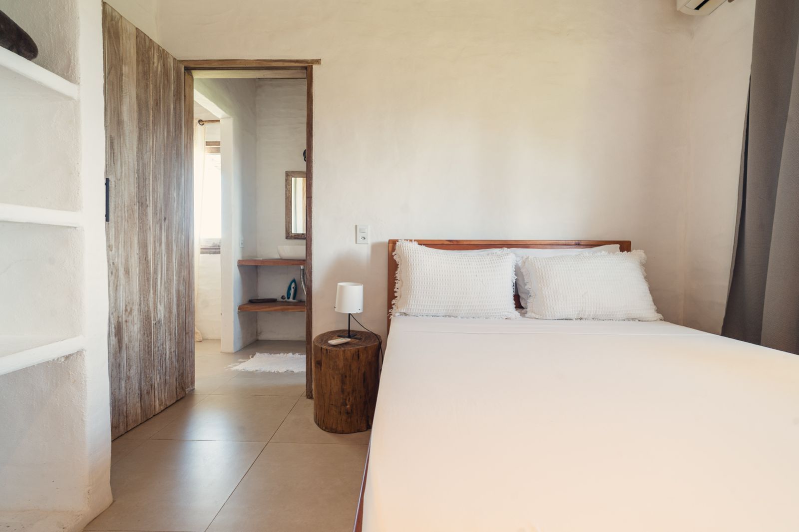 Ein Schlafzimmer mit einem Bett, einem Nachttisch, einem Spiegel und einer Holztür.