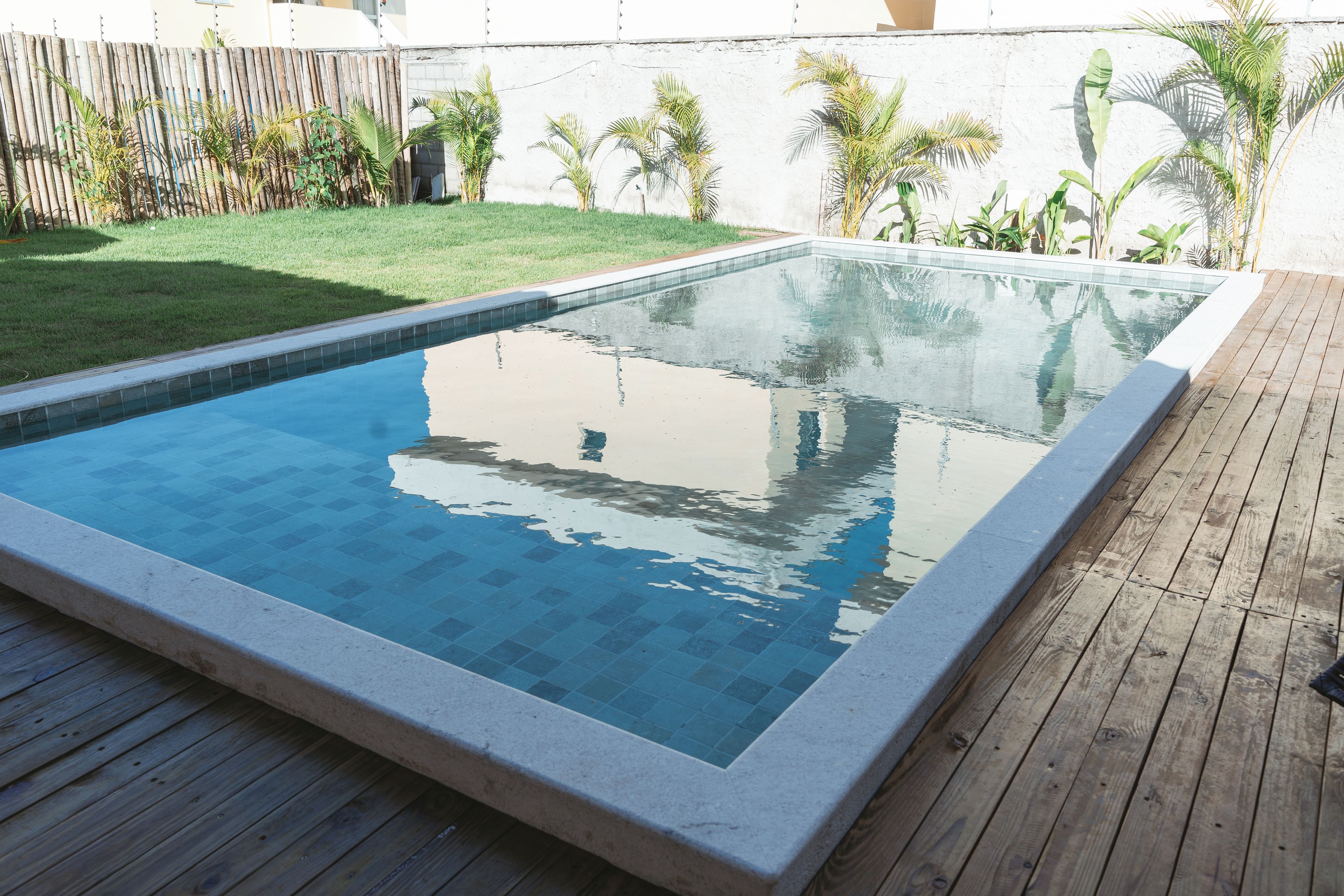 Una piscina rectangular con borde de azulejos, rodeada por un muelle de madera y una zona ajardinada con plantas pequeñas.
