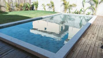 Una piscina rectangular con borde de azulejos, rodeada por un muelle de madera y una zona ajardinada con plantas pequeñas.