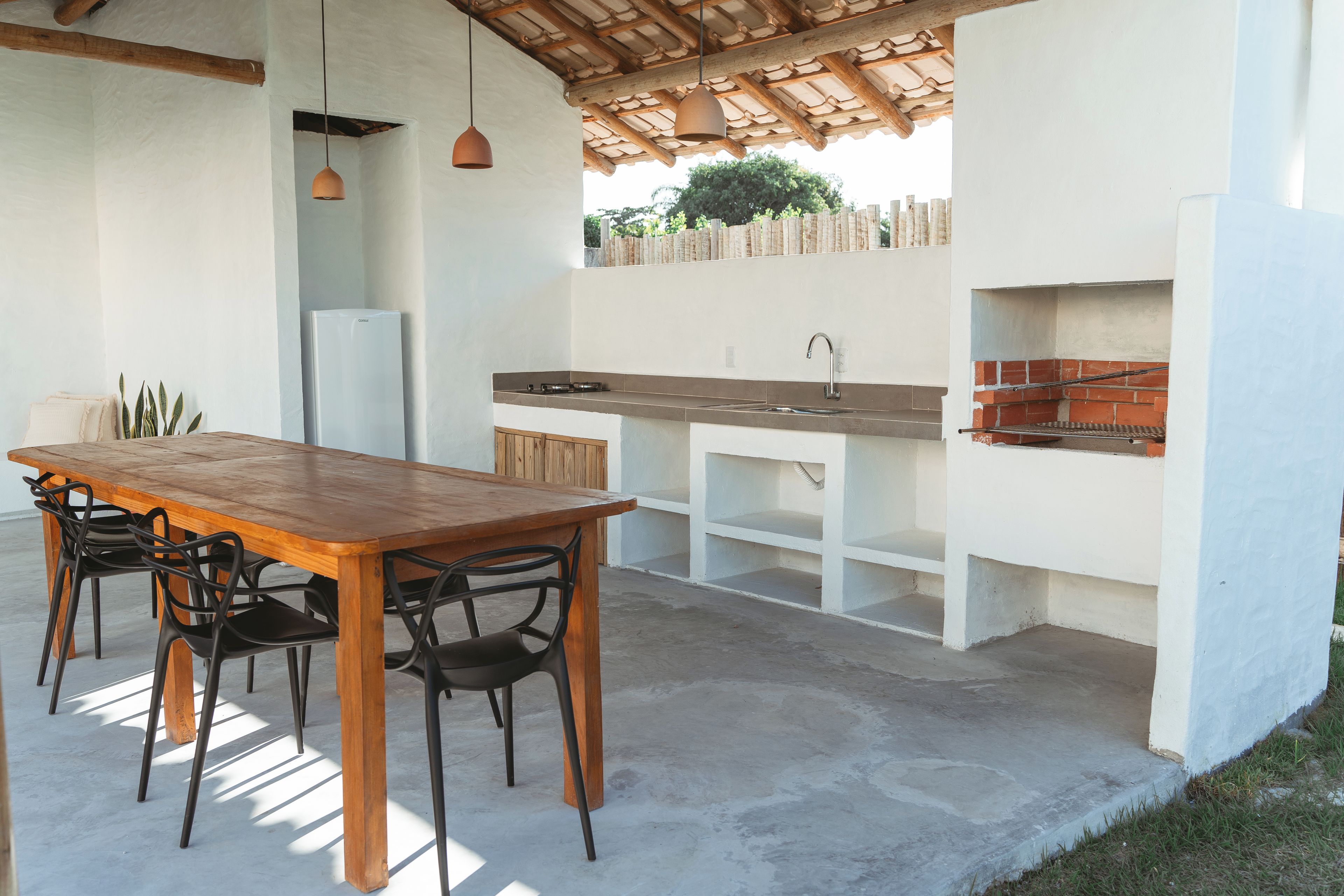 Een buitenkeuken met een houten tafel en stoelen, een gootsteen en een barbecue.