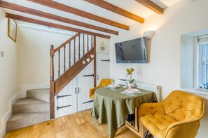 A room with a wooden staircase, a dining table with chairs, a television mounted on the wall, and a window with blinds. - 1 Bed in Talgarreg (oc-t46321) (Talgarreg)