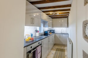 A modern kitchen with white cabinets, a black countertop, and a wooden ceiling. - 1 Bed in Talgarreg (oc-t46321) (Talgarreg)