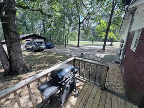 A wooden deck with a grill, a covered carport, and a brick building. - The Parkway House: A peaceful 3-bedroom house on top of Lookout Mountain (Fort Payne)