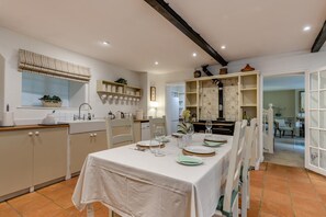 A dining area with a table set for four, kitchen cabinets, a window with a curtain, and a tiled floor. - 2 Bed in Stoke Hammond (oc-o46350) (Stoke Hammond)