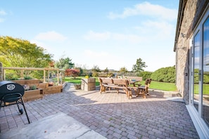 An outdoor patio with a barbecue grill, wooden furniture, and a garden view. - 4 Bed in Chathill (oc-e42807) (Ellingham)