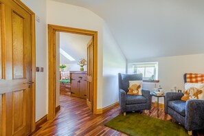 A room with a wooden door, a chair with a cushion, a small table with a cup, and a window with a view. - 4 Bed in Chathill (oc-e42807) (Ellingham)