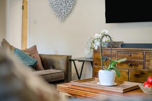 Ein Wohnzimmer mit einer Couch, einem Couchtisch mit Pflanze, einem Holzschrank und einem Fernseher an der Wand.