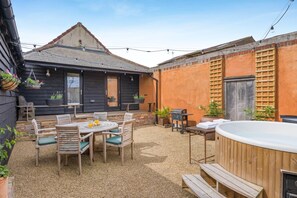 Eine Terrasse mit einem runden Tisch, Stühlen, einem Whirlpool und einem Grill.