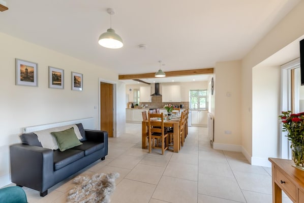 A modern living room with a sofa, a dining area with a table and chairs, and a kitchen in the background. - 5 Bed in Newbridge-on-Wye (oc-u46325) (Newbridge on Wye)