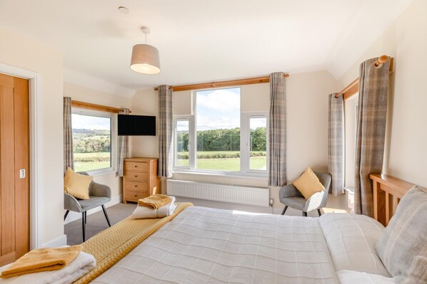Ein Schlafzimmer mit einem großen Bett, zwei Stühlen, einer Kommode, einem Fernseher und einem Fenster mit Blick ins Freie.