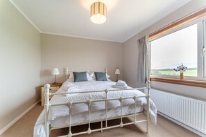 A bedroom with a bed, bedside lamps, a window with a view, and a radiator.
