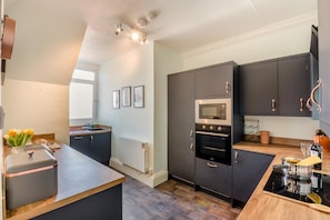 A modern kitchen with dark cabinetry, a built-in oven, a microwave, and a wooden countertop. - 2 Bed in Whitby (oc-s46340) (Whitby)