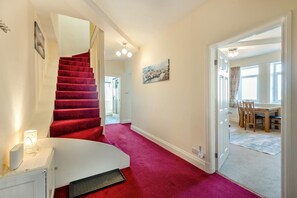 A hallway with a red carpet, a white radiator, a staircase, and a dining area with a table and chairs. - 2 Bed in Whitby (oc-s46340) (Whitby)
