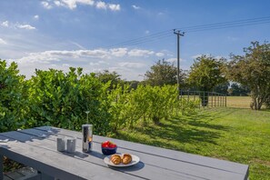 An outdoor dining area with a table set for two, a metal pitcher, and a bowl of strawberries. - 3 Bed in Roughton (oc-e46003) (Roughton)
