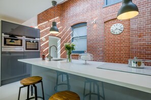 Cozinha moderna com parede de tijolos, bancada branca e banquetas.