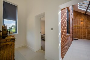 Quarto com escrivaninha de madeira, janela com vista, parede de tijolos e claraboia.