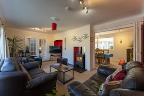 Ein Wohnzimmer mit Ledersofas, einem Fernseher, einem Kamin und einem Essbereich mit Tisch und Stühlen.