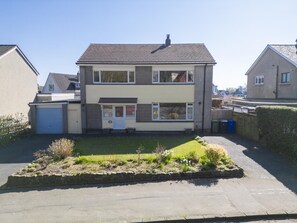 Ein zweigeschossiges Wohnhaus mit Garage und Garten vor der Fassade, bewölkter Himmel.