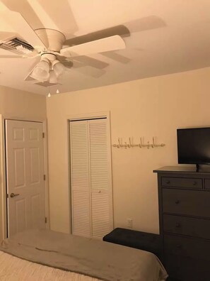 Ein Schlafzimmer mit einem Bett, einem Schminktisch, einem Fernseher, einem Deckenventilator und einem Kleiderschrank.