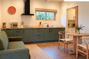 A modern kitchen with a built-in oven, a window with a view, and a dining area with a wooden table and chairs. - Mid-Century Studio in Woodland Hills (Los Angeles)
