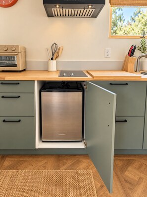 Una cocina compacta con refrigerador integrado, un tostador y una ventana con vistas a árboles.