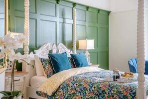 A four-poster bed with a floral bedspread, a nightstand with a lamp, and a tray with pastries. - 3 Bed in Penpedairheol (oc-o46341) (Penpedairheol)