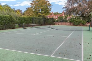 Ein Tennisplatz mit Netz, umzäunt und von Bäumen gesäumt.