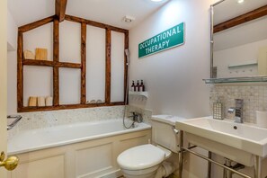 Ein Badezimmer mit Holzbalkendecke, einem Schild für Ergotherapie, einer Badewanne, einer Toilette und einem Waschbecken mit Toilettenartikeln.