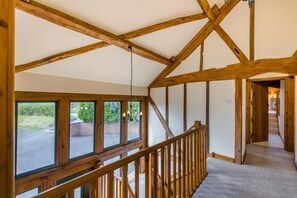 A room with a sloped ceiling, wooden beams, a staircase with a wooden railing, and large windows with a view of greenery outside. - 4 Bed in Rhayader (oc-c46317) (Rhayader)