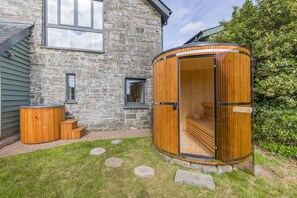 A stone building with a wooden sauna structure, a hot tub, and a small outdoor seating area. - 4 Bed in Rhayader (oc-c46317) (Rhayader)