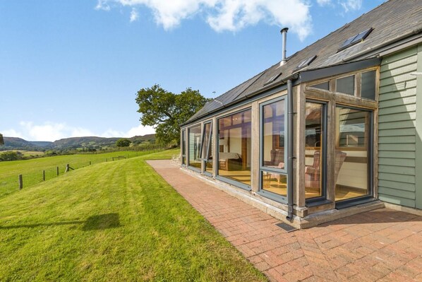 A house with a glass conservatory, a brick pathway, and a grassy yard. - 4 Bed in Rhayader (oc-c46317) (Rhayader)