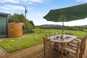 A wooden deck with a round table and chairs, a large umbrella, and a hot tub. - 4 Bed in Rhayader (oc-c46317) (Rhayader)