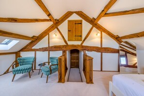 A loft bedroom with exposed wooden beams, a skylight, a staircase, and two checkered armchairs. - 4 Bed in Rhayader (oc-c46317) (Rhayader)