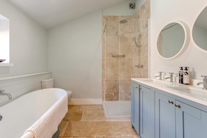 Une salle de bain moderne avec une baignoire sur pieds, une douche à l’italienne et un meuble-lavabo doté d’un miroir et d’articles de toilette.