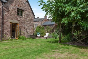 A stone house with a grassy yard, two white chairs, and a wooden table. - 1 Bed in Blakeney (oc-a46334) (Blakeney)