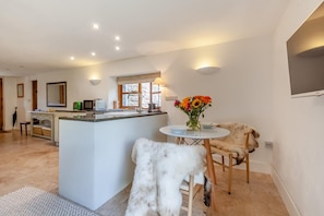 A modern kitchen with a central island, a dining area with a white table and chairs, and a large window providing natural light. - 1 Bed in Blakeney (oc-a46334) (Blakeney)