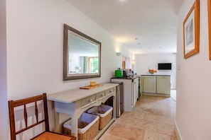 A hallway leading to a kitchen with a mirror, a wooden bench, and a console table with baskets. - 1 Bed in Blakeney (oc-a46334) (Blakeney)