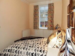 Un dormitorio con cama, ventana con cortinas, radiador y mesita de noche con lámpara.