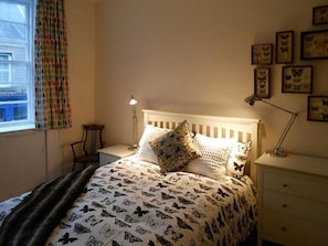 Ein Schlafzimmer mit einem Bett, einem Nachttisch, einer Lampe, einem Fenster mit Vorhängen und Wandbildern mit Schmetterlingsmotiv.