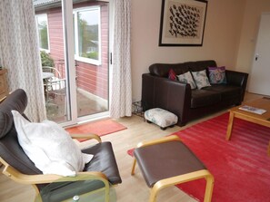 A living room with a sofa, a chair, a coffee table, and a sliding glass door leading to an outdoor area. - 4 Bed in Kirkcudbright (oc-d546533) (Kirkcudbright)