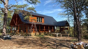 Eine Holzhütte mit Veranda, einer Leiter und einem Picknicktisch inmitten von Bäumen.