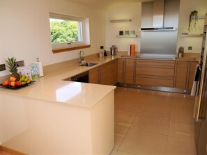 A modern kitchen with a central island, stainless steel appliances, and a window overlooking greenery. - 4 Bed in Portpatrick (oc-d587345) (Portpatrick)