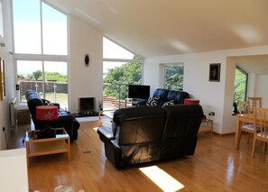 A spacious living room with a fireplace, a sofa, a television, and a balcony with a view of greenery. - 4 Bed in Portpatrick (oc-d587345) (Portpatrick)