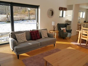 Ein Wohnzimmer mit einer Couch, einem Sessel, einem kleinen Tisch und Blick auf eine verschneite Landschaft durch große Fenster.